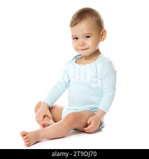 Adorable petit garçon curieux dans une barboteuse est assis et souriant sur fond blanc. Banque D'Images