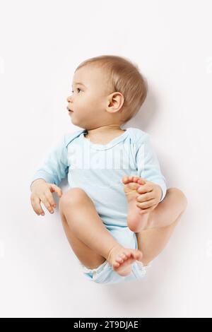 Adorable petit garçon dans une barboteuse est allongé sur le dos et regardant sur fond blanc. Banque D'Images