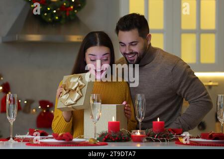 Surprise jeune femme ouvrant cadeau de Noël de son petit ami à la table dans la cuisine Banque D'Images