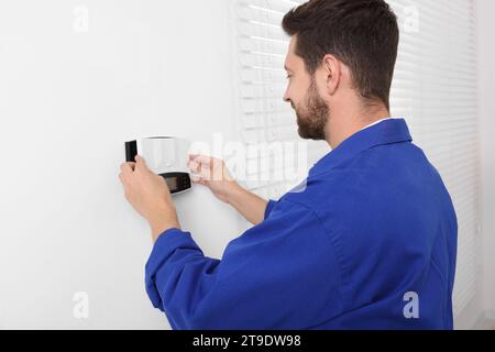 Technicien installant le système d'alarme de sécurité à domicile sur le mur blanc à l'intérieur Banque D'Images