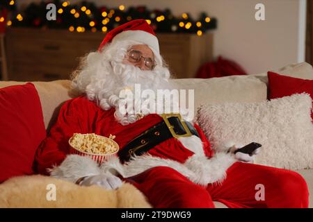 Joyeux Noël. Père Noël avec seau de pop-corn dormir tout en regardant la télévision sur le canapé à la maison Banque D'Images