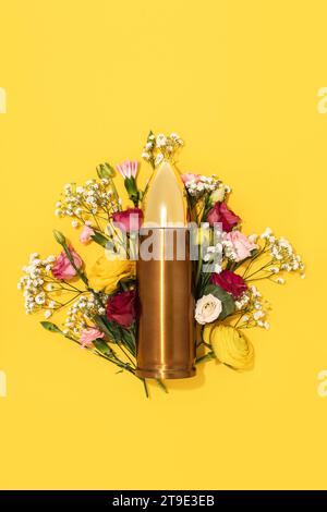 Pacifisme et mouvement de non-violence. Grosse balle et bouquet de fleurs différentes sur fond jaune. Banque D'Images