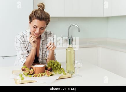 Jeune jolie femme prête à manger son délicieux yaourt grec avec des figues dans la cuisine blanche Banque D'Images