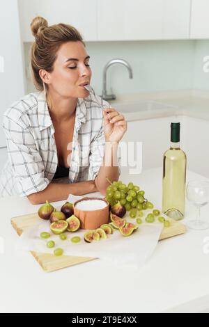 Jeune jolie femme prête à manger son délicieux yaourt grec avec des figues dans la cuisine blanche Banque D'Images