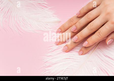 Gros plan des mains féminines avec la peau lisse et plume d'autruche douce sur fond rose Banque D'Images