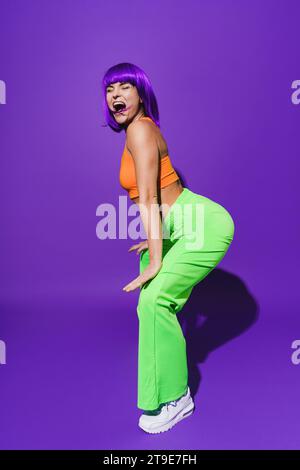 Danseuse insouciante portant des vêtements de sport colorés twerking sur fond violet Banque D'Images