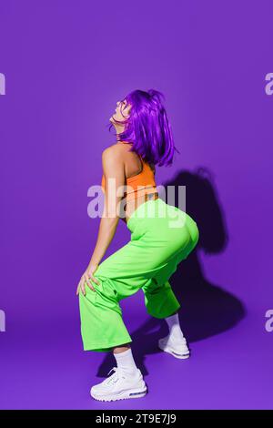 Danseuse insouciante portant des vêtements de sport colorés twerking sur fond violet Banque D'Images