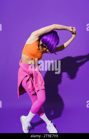 Jeune danseuse insouciante portant des vêtements de sport colorés exécutant sur fond violet Banque D'Images