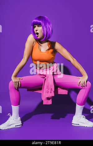 Jeune danseuse insouciante portant des vêtements de sport colorés exécutant sur fond violet Banque D'Images