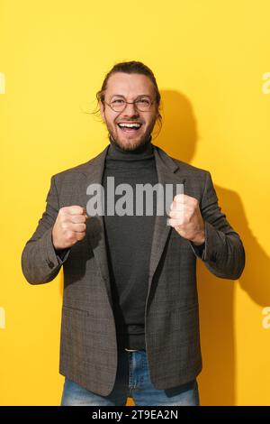 Jeune homme joyeux et réussi portant des lunettes sur fond jaune Banque D'Images