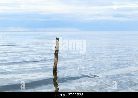 Un beau plan d'un paysage de mer calme avec poteau de jetée cassé sortant de l'eau sur le fond d'horizon. Banque D'Images