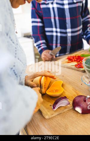 Section médiane de divers couples seniors tranchant la courge butternut, hachant les légumes dans la cuisine Banque D'Images