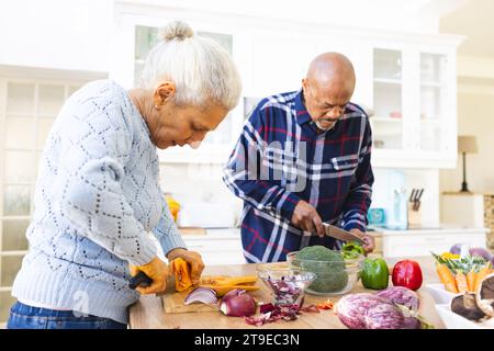 Divers couples seniors tranchant la courge butternut, coupant les légumes dans la cuisine Banque D'Images