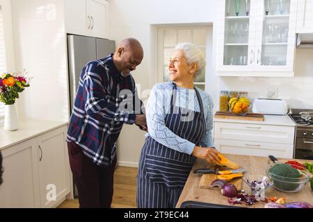 Heureux couple senior diversifié tranchant la courge butternut, hachant les légumes dans la cuisine Banque D'Images