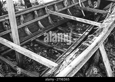 Gros plan en noir et blanc d'un vieux bateau de pêche endommagé et abandonné reposant sur le rivage. Banque D'Images