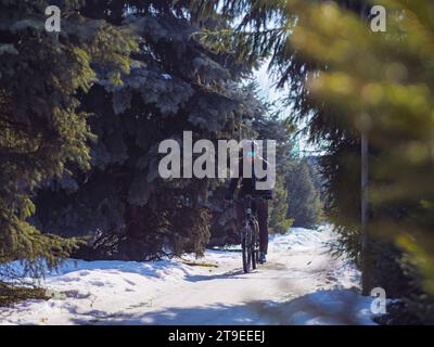Un jeune homme fait du vélo en hiver dans un parc de la ville. Passe-temps actif en hiver. Vélo comme transport écologique pour toutes les saisons Banque D'Images