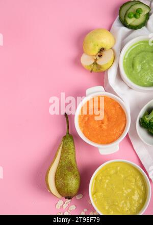 Purée de légumes et de fruits pour bébés dans des bols blancs avec des ingrédients sur fond rose. Concept d'aliments pour bébés. Vue de dessus. Banque D'Images