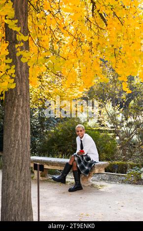 Jeune homme souriant à la caméra assis sur le banc du parc interagissant avec le téléphone portable, photo verticale Banque D'Images