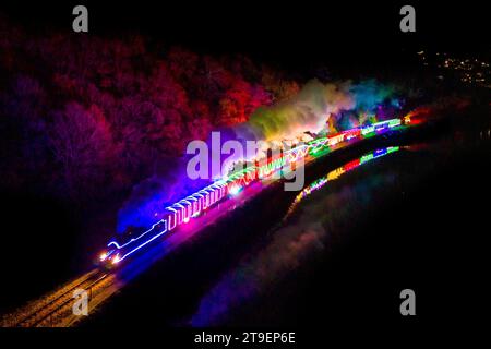 Kingswear, Devon, Royaume-Uni. 24 novembre 2023. Le train des lumières de Noël sur le chemin de fer à vapeur de Dartmouth dans le Devon, qui circule entre le 24 novembre et le 30 décembre 2023, se dirige vers Paignton alors qu'il voyage à côté de la rivière Dart après avoir quitté Kingswear. Les voitures et les locomotives à vapeur du service festif sont éclairées à l'intérieur et à l'extérieur avec des lumières colorées. Crédit photo : Graham Hunt/Alamy Live News Banque D'Images