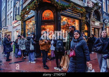 Amsterdam, pays-Bas. 24 novembre 2023. Les gens attendent devant le magasin Van Wonderen Stroopwafels, qui vend des bonbons traditionnels hollandais. À Amsterdam, les magasins sont prêts avec des offres Black Friday, et les vitrines des magasins sont décorées avec des bannières de vente pour attirer les gens pendant le Black Friday. Les plus jeunes, en particulier, attendent le jour de réduction après Thanksgiving de l'Amérique pour acheter des choses. Crédit : SOPA Images Limited/Alamy Live News Banque D'Images