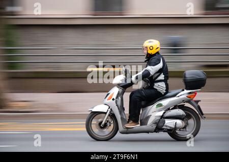 Belgrade, Serbie- 23 novembre 2023 : un homme conduit un scooter gris avec coffre arrière de rangement dans la rue de la ville, panoramique Banque D'Images