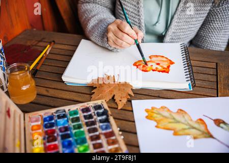 Peinture à l'aquarelle. Femme artiste peint un thème d'automne sur papier. Palette de couleurs sur la table Banque D'Images