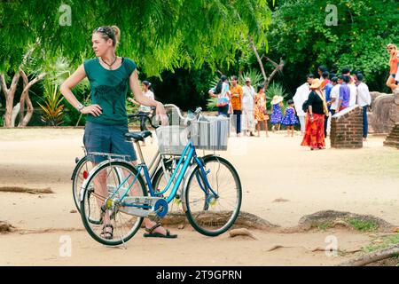 Une touriste se tient debout avec son vélo pendant que la population locale explore les ruines de Polonnaruwa au Sri Lanka Banque D'Images