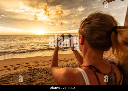 Une femme blonde prend une photo du coucher de soleil à l'horizon à Negombo au Sri Lanka Banque D'Images