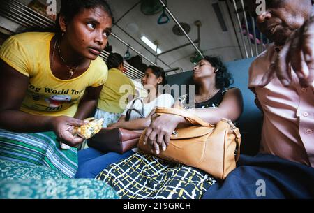Une femme portant un t-shirt jaune tente de vendre des noix à un passager dans un train au Sri Lanka Banque D'Images