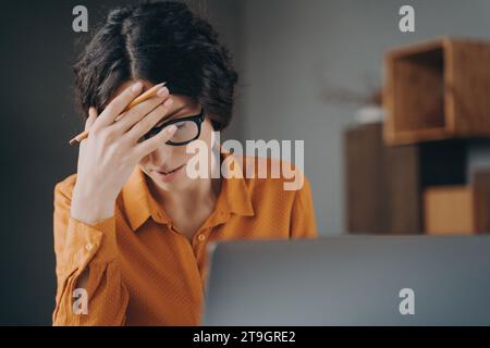 Femme concentrée avec des lunettes ressent un mal de tête pendant le travail sur son ordinateur portable. Banque D'Images