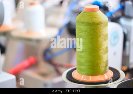 Bobine de fil sur une machine à coudre industrielle dans une usine de confection, fond textile industriel Banque D'Images