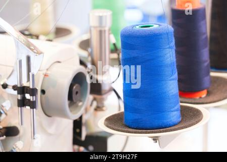 Bobine de fil sur une machine à coudre industrielle dans une usine de confection, fond textile industriel Banque D'Images