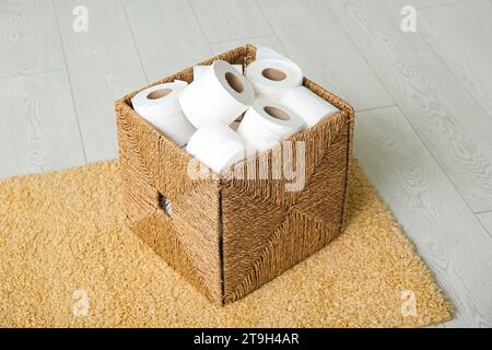 Panier en osier avec rouleaux de papier toilette sur le sol Banque D'Images