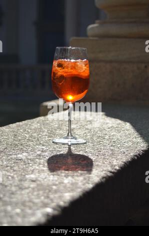 Un Aperol Spritz dans un verre à vin à la lumière naturelle sur un rebord en pierre dans la cour d'un palais italien à Milan, Italie Banque D'Images