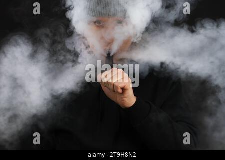 Les hommes fument une cigarette électronique sur le fond sombre. Mise au point sélective Banque D'Images