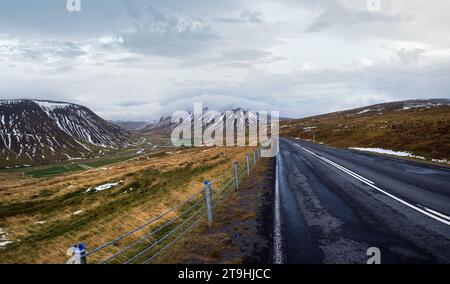 Route d'autoroute et vue sur la montagne lors d'un voyage en voiture en Islande. Paysage islandais spectaculaire avec une nature pittoresque : montagnes des highlands, champs, nuages, g Banque D'Images