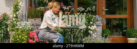 Une femme souriante professionnelle fleuriste regardant un ordinateur portable a commandé à son bureau dans sa boutique de fleurs Banque D'Images