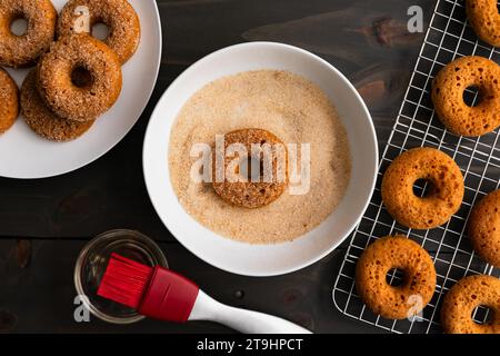 Tremper des donuts au cidre de pomme cuits dans du sucre de cannelle : beignet cuit dans un bol peu profond rempli de sucre de canne biologique et de cannelle moulue Banque D'Images