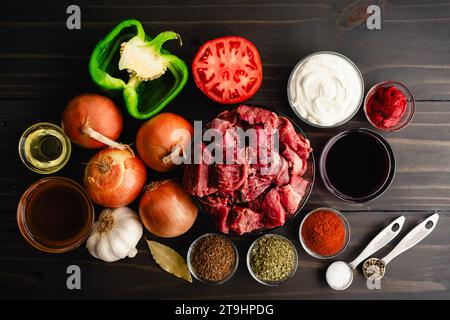 Goulash allemand Ingrédients sur une table en bois foncé fond : viande de ragoût, légumes et épices utilisés pour faire un goulash de bœuf mijoté Banque D'Images