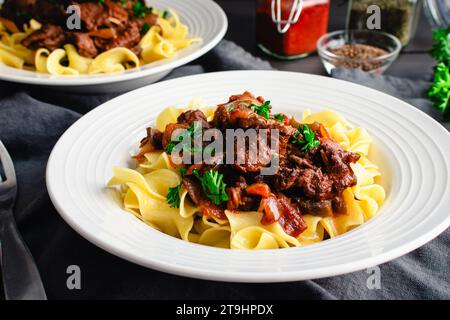 Goulash allemand servi sur des nouilles aux œufs dans un bol peu profond : morceaux de bœuf mijotés assaisonnés de marjolaine, de graines de carvi et de paprika Banque D'Images