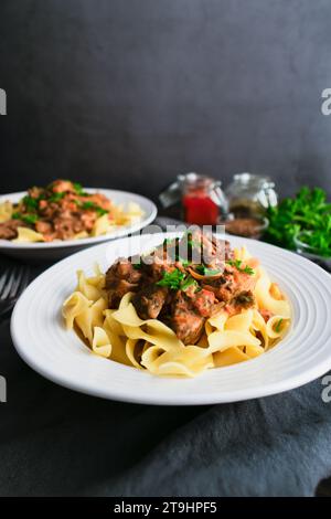 Goulash allemand servi sur des nouilles aux œufs dans un bol peu profond : morceaux de bœuf mijotés assaisonnés de marjolaine, de graines de carvi et de paprika Banque D'Images