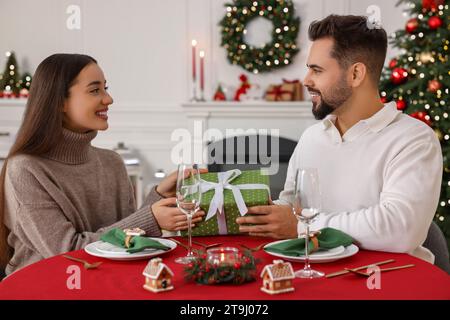 Heureux jeune homme présentant cadeau de Noël à sa petite amie à table à l'intérieur Banque D'Images