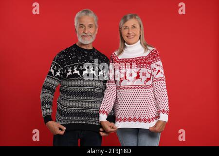 Couple senior montrant des pulls de Noël sur fond rouge Banque D'Images