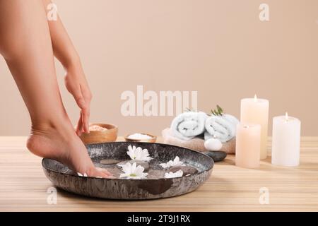 Femme trempant son pied dans un bol avec de l'eau et des fleurs de chrysanthème sur une surface en bois, gros plan. Procédé de pédicure Banque D'Images