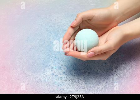 Femme tenant la bombe de bain au-dessus de l'eau avec de la mousse, gros plan. Espace pour le texte Banque D'Images