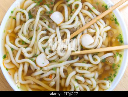 Gros plan vue de dessus plat d'un bol de nouilles udon dans le bouillon de boeuf. Hacher les bâtonnets dans le bol. Banque D'Images