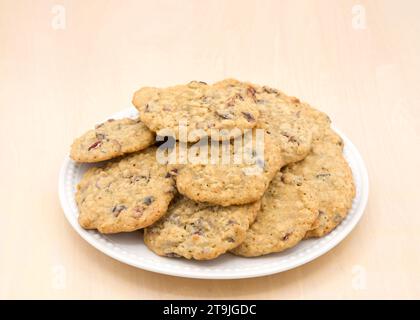 Gros plan sur une assiette en porcelaine pleine de biscuits à la canneberge à l'avoine sur un fond de table en bois clair. Banque D'Images