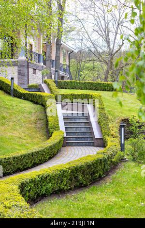 Un escalier en pierre avec des marches en granit monte le long des buissons de buis taillés à un beau domaine avec en toile de fond la verdure du parc. Banque D'Images