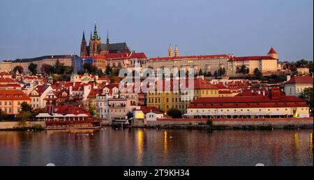 Château de Prague sur une colline avec les bâtiments environnants et la rivière sous un ciel rosâtre. Banque D'Images