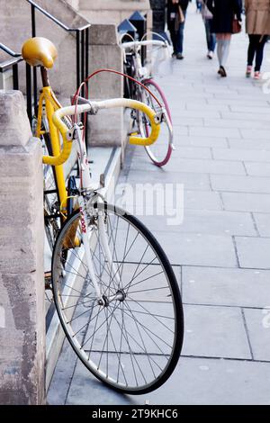 Vélo jaune appuyé contre un mur à Londres avec des piétons anonymes marchant le long du trottoir dans l'arrière-plan lointain Banque D'Images